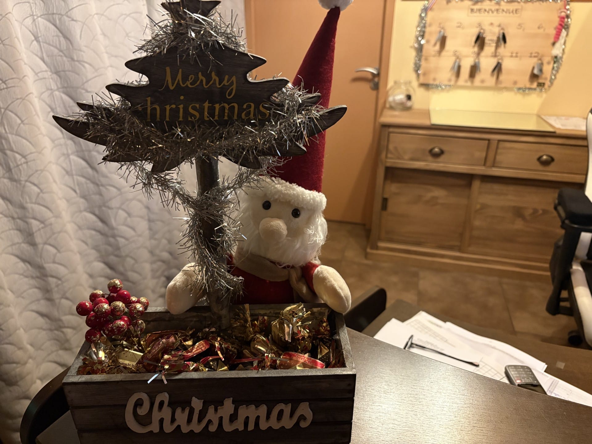 Petit Père Noël en peluche et boîte en bois remplie de friandises. Un sapin décoratif porte l'inscription "Merry Christmas".
